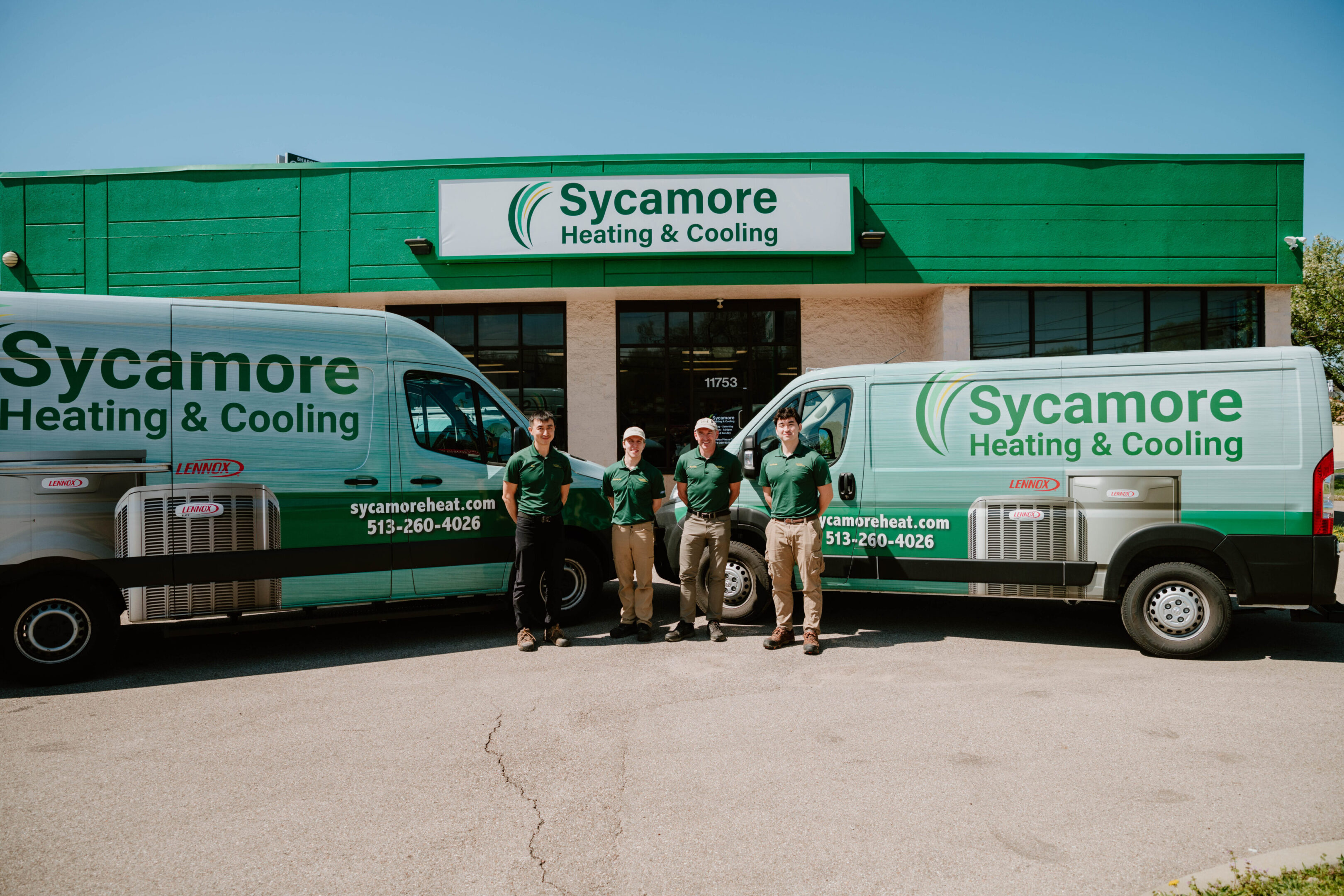 Three men standing in front of a building with two vans.